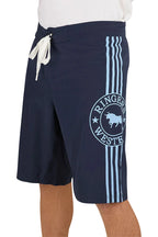 A person wears Ringers Western Mens Southern Cross Swim Shorts (124085RW) NSW—navy with light blue stripes, a circular Ringers Western bull logo on the left leg, white drawstring, and made from recycled polyester.