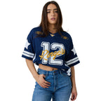 A woman modeling a navy blue sports jersey tucked up with '12 Ringers' in white and gold script, paired with blue jeans, against a white studio background.