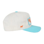 A white baseball cap with a light blue visor and matching light blue button, featuring a small orange bull logo and a blue-bordered patch on the side.