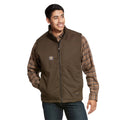 A man smiles with one hand in his pocket, wearing an Ariat Mens F20 Rebar Duracanvas Vest (10027851) in Wren over a plaid shirt and jeans, standing against a plain white background.