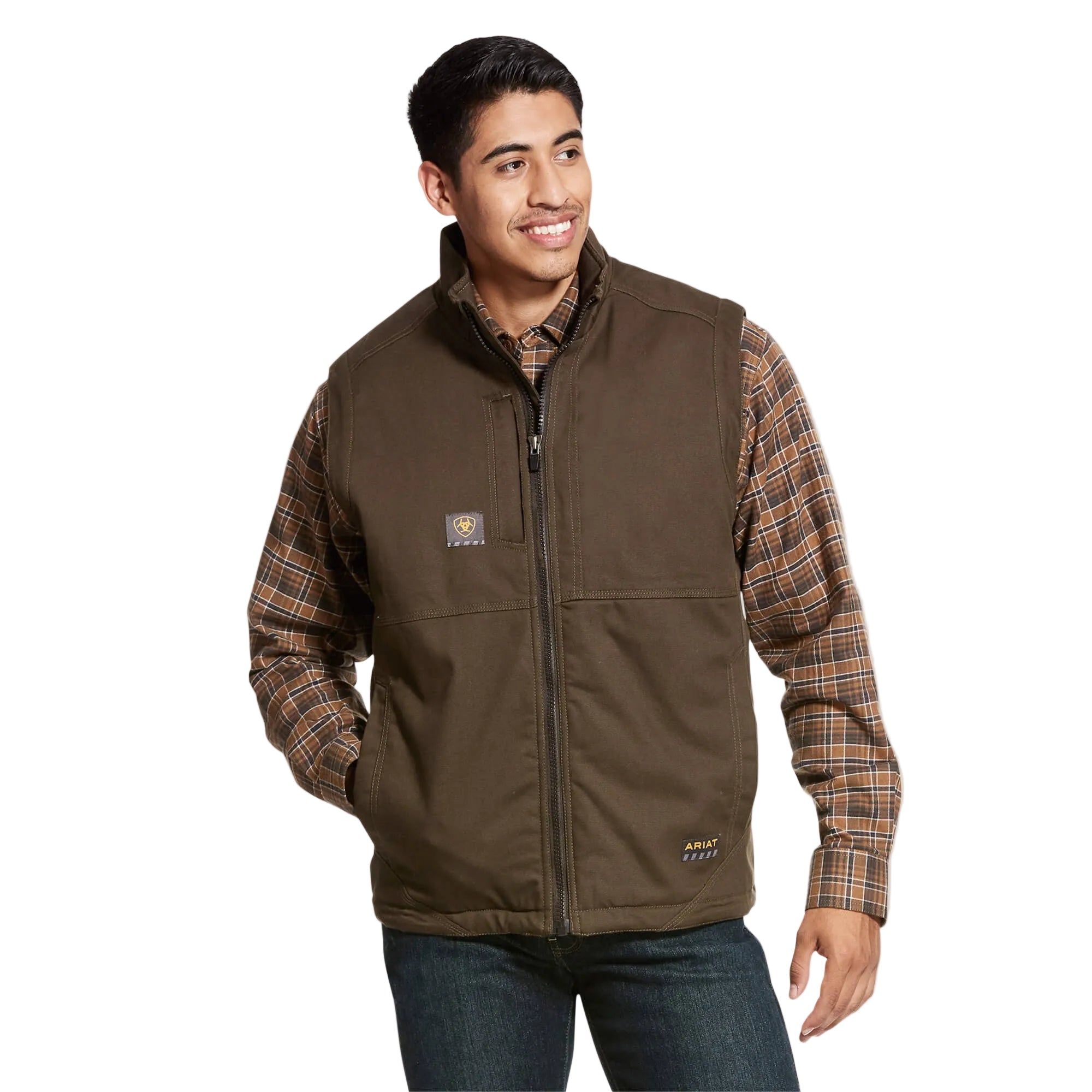 A man smiles with one hand in his pocket, wearing an Ariat Mens F20 Rebar Duracanvas Vest (10027851) in Wren over a plaid shirt and jeans, standing against a plain white background.