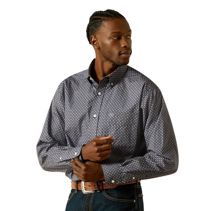 A man wearing a navy Ariat Men's Wrinkle Free Dale L/S Shirt (10062195) with a small white geometric pattern, paired with a brown western belt and blue jeans, against a solid white background.
