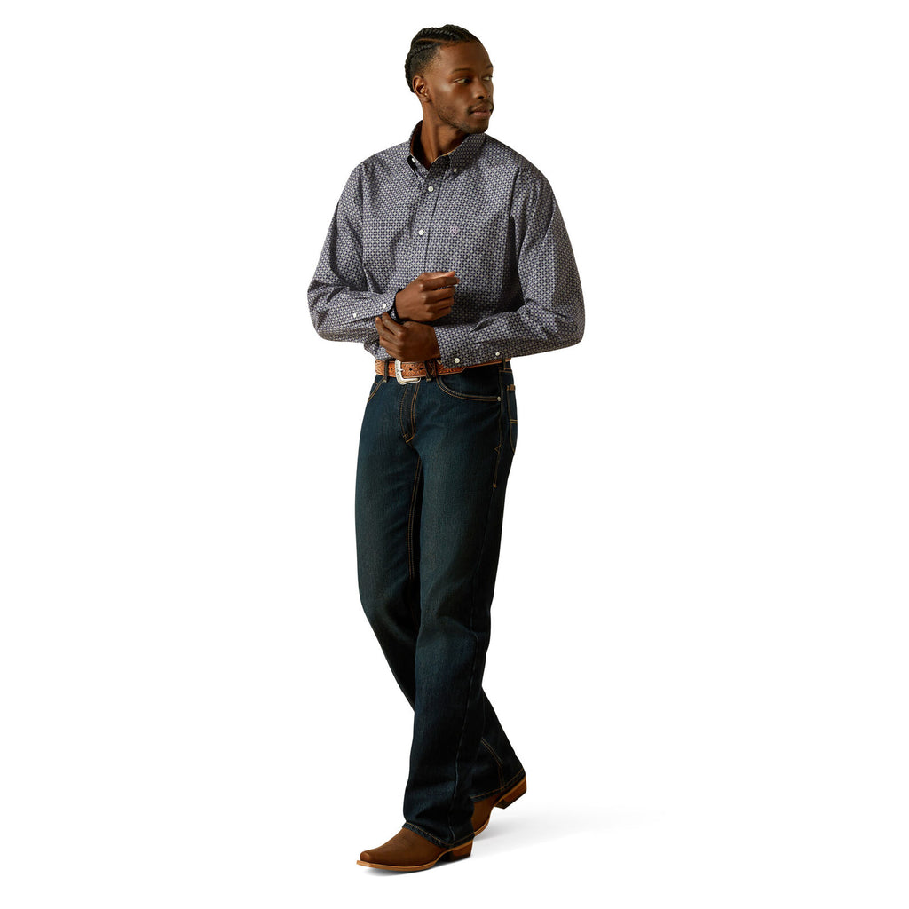 A man wearing a navy Ariat Men's Wrinkle Free Dale L/S Shirt (10062195) with a small white geometric pattern, paired with a brown western belt and blue jeans, against a solid white background.
