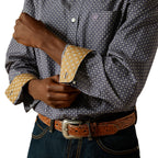Close up of a man wearing a navy Ariat Men's Wrinkle Free Dale L/S Shirt (10062195) with a small white geometric pattern showing cuff detail, paired with a brown western belt and blue jeans, against a solid white background.