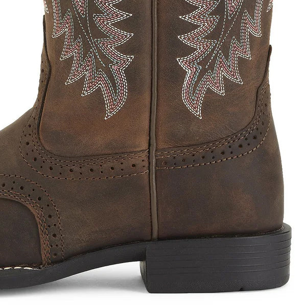 Close-up of a brown leather cowboy boot with decorative white and red stitching, perforated details, and a black, low-heeled sole.