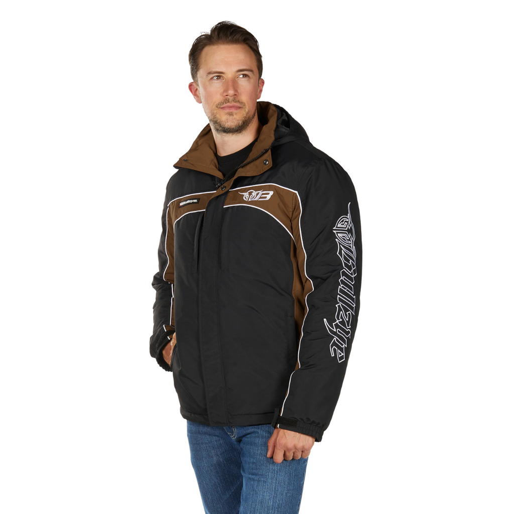 A man wearing a Bullzye Mens Bazooka Jacket (B6W1704039) in Black/Dark Tan with white accents, featuring logos and lettering on the chest and sleeve, stands in blue jeans with one hand in his pocket, looking slightly to the side.