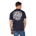 A man in the Bullzye Mens Brew S/S Tee (B6W1503507) Navy, featuring a bold white "BULLZYE" logo and text on the back, pairs it with blue jeans and stands with his head turned to the side.
