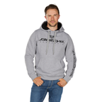 A man wears the Bullzye Mens Determination Hoodie (B6W1512502) in grey marle, featuring chest and sleeve branding, with one hand in his jeans pocket against a white background.