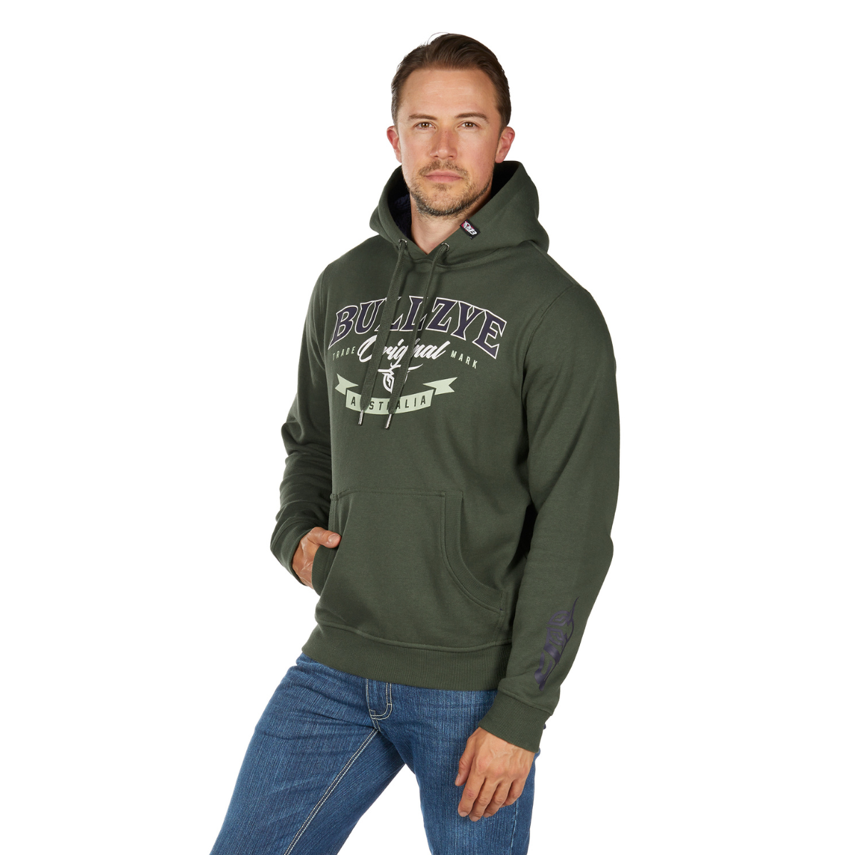 A man in a Bullzye Mens Original Hoodie (B6W1512503) Green, featuring "BULLZYE" text on the chest, stands with one hand in his pocket and the other by his side, wearing blue jeans against a white background.