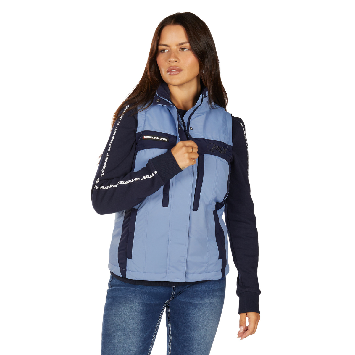 A woman with long brown hair wears the Bullzye Womens Carla Vest (B6W2609529) Navy/Light Blue over a navy long-sleeve shirt and blue jeans, looking slightly left against a white background.