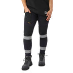 A woman from the waist down wearing navy blue CAT Women's Taped Work Stretch Leggings (1810096) with hi vis taping on the lower legs, paired with a black tee and honey coloured work boots, on a white background.