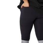 A close up of a woman from the waist down wearing navy blue CAT Women's Taped Work Stretch Leggings (1810096) with hi vis taping on the lower legs, showing the pocket detail, paired with a black tee on a white background.