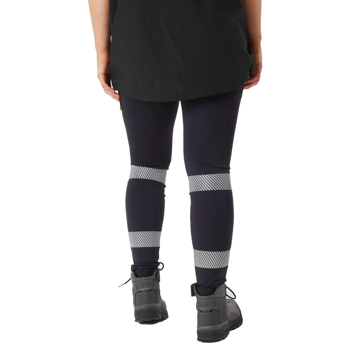 A woman viewed from behind, from the waist down wearing navy blue CAT Women's Taped Work Stretch Leggings (1810096) with hi vis taping on the lower legs, paired with a black tee and honey coloured work boots, on a white background.