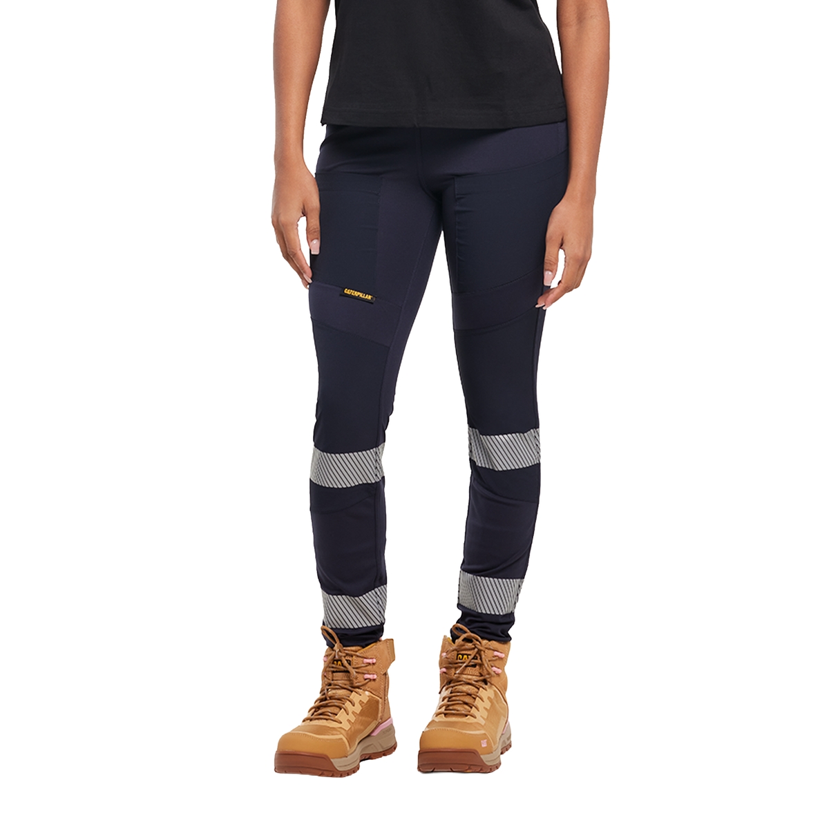 A woman from the waist down wearing navy blue CAT Women's Taped Work Stretch Leggings (1810096) with hi vis taping on the lower legs, paired with a black tee and honey coloured work boots, on a white background.