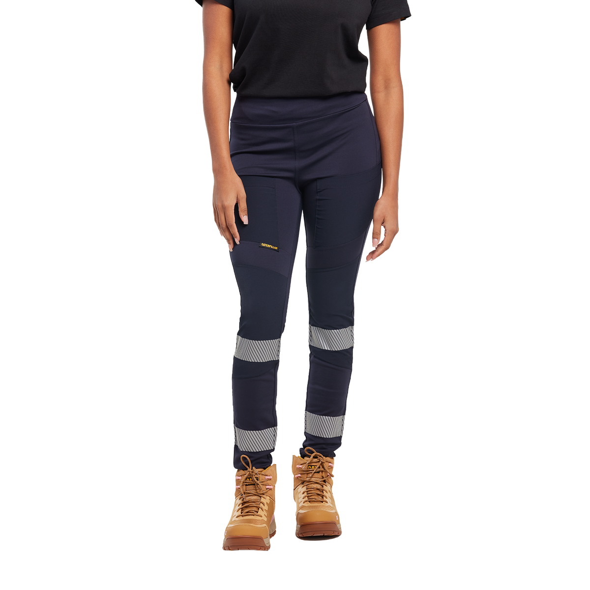 A woman from the waist down wearing navy blue CAT Women's Taped Work Stretch Leggings (1810096) with hi vis taping on the lower legs, paired with a black tee and honey coloured work boots, on a white background.