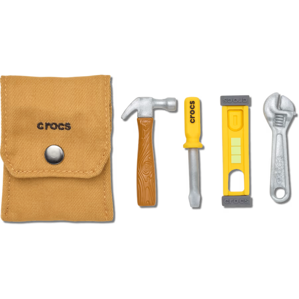 A tan fabric pouch labeled "crocs" is next to Crocs Tool Kit 5 Pack Jibbitz Shoe Charms: a brown hammer, yellow screwdriver with "crocs," yellow and gray level, and silver wrench, all arranged in a row.