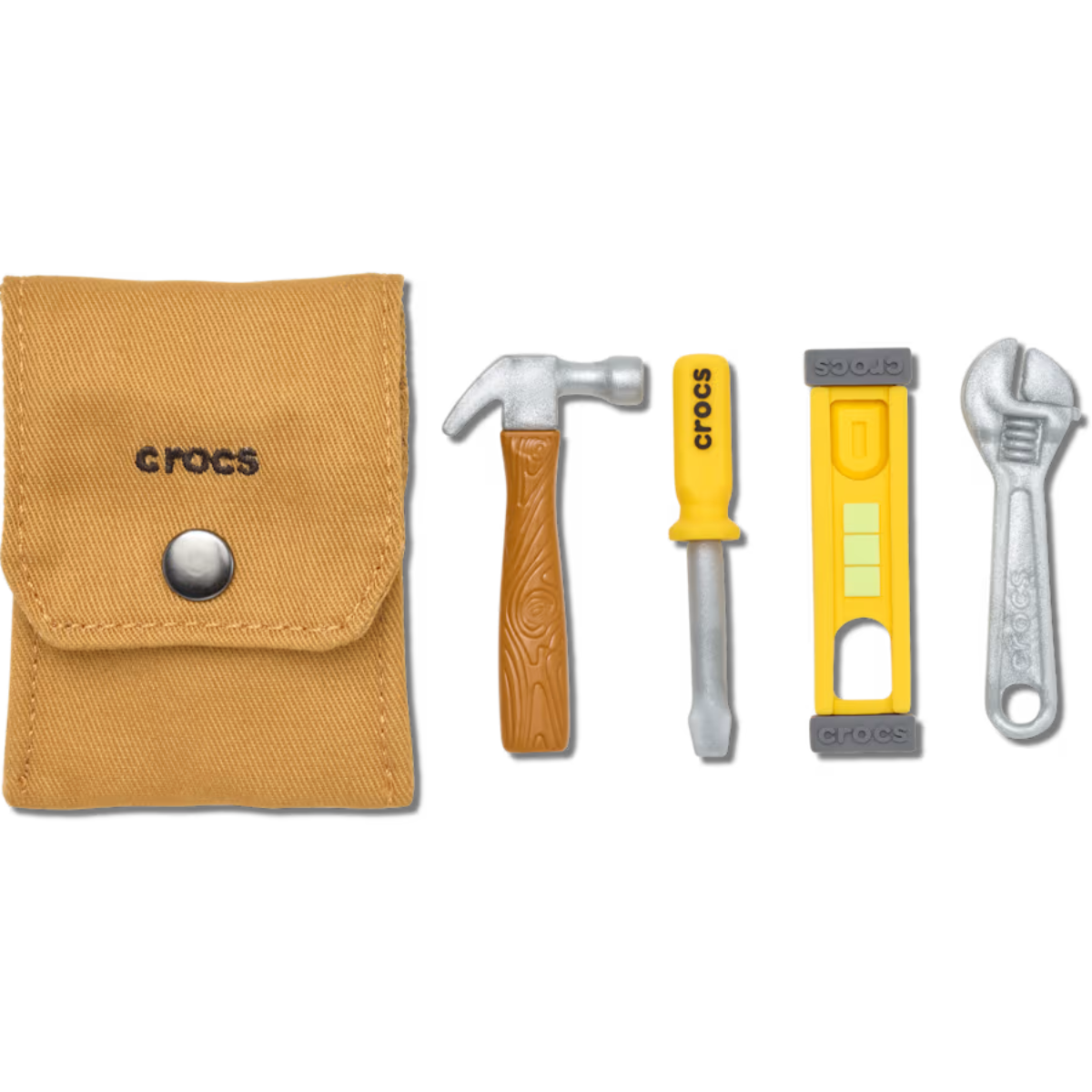 A tan fabric pouch labeled "crocs" is next to Crocs Tool Kit 5 Pack Jibbitz Shoe Charms: a brown hammer, yellow screwdriver with "crocs," yellow and gray level, and silver wrench, all arranged in a row.