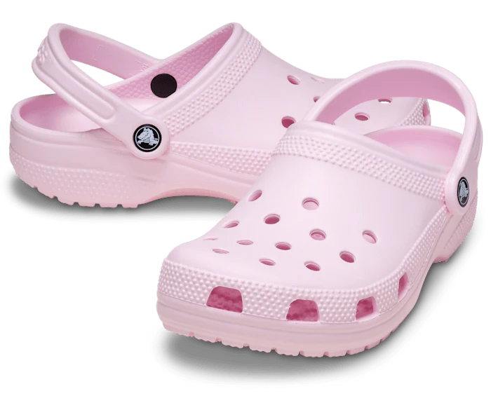 The Crocs Unisex Classic Clogs (10001-6ZW) Pink Milk feature ventilation holes, adjustable heel straps, and cushioned comfort. These water-friendly Crocs are shown in light pink on a white background.