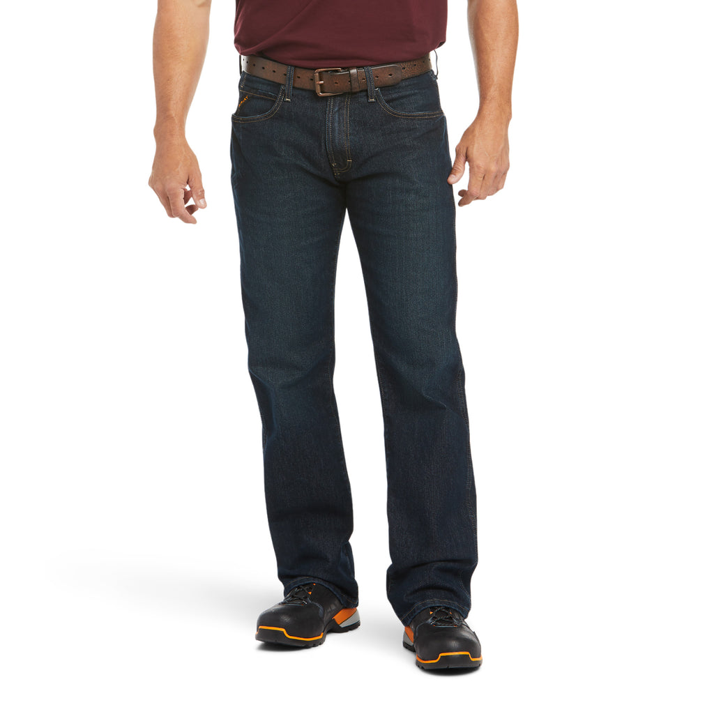 A man, face not visible, stands against a white background wearing a maroon shirt, brown belt, black work boots, and Ariat Rebar M5 Jeans (10016223) Blackstone by Ariat.