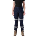 A woman wearing a pair of navy blue FXD Women's Cuffed Taped Work Pants (WP-8WT) with reflective silver-grey bands on the legs, paired with a black t-shirt and stone coloured boots, against a plain white background.