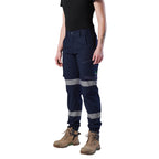 A 3-4 front view of a woman wearing a pair of navy blue FXD Women's Cuffed Taped Work Pants (WP-8WT) with reflective silver-grey bands on the legs, paired with a black t-shirt and stone coloured boots, against a plain white background.