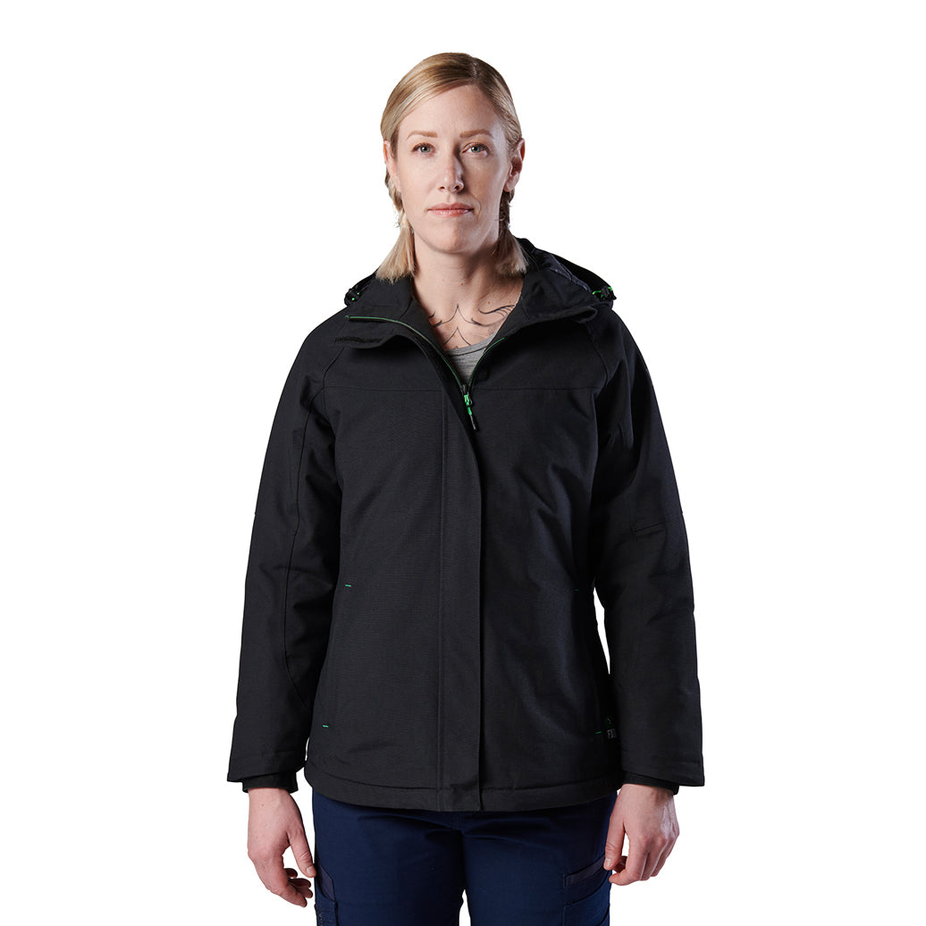 A woman modelling a black hooded FXD Women's WO-1W Insulated Waterproof Jacket (FX12407001) with a full front zipper and zippered chest pocket, paired with dark blue pants, against a solid white background.