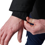 Close-up of a woman modelling a black hooded FXD Women's WO-1W Insulated Waterproof Jacket (FX12407001) showing hands and a black elastic wrist cuff on a black jacket sleeve, with a dark navy garment visible underneath against a white background.