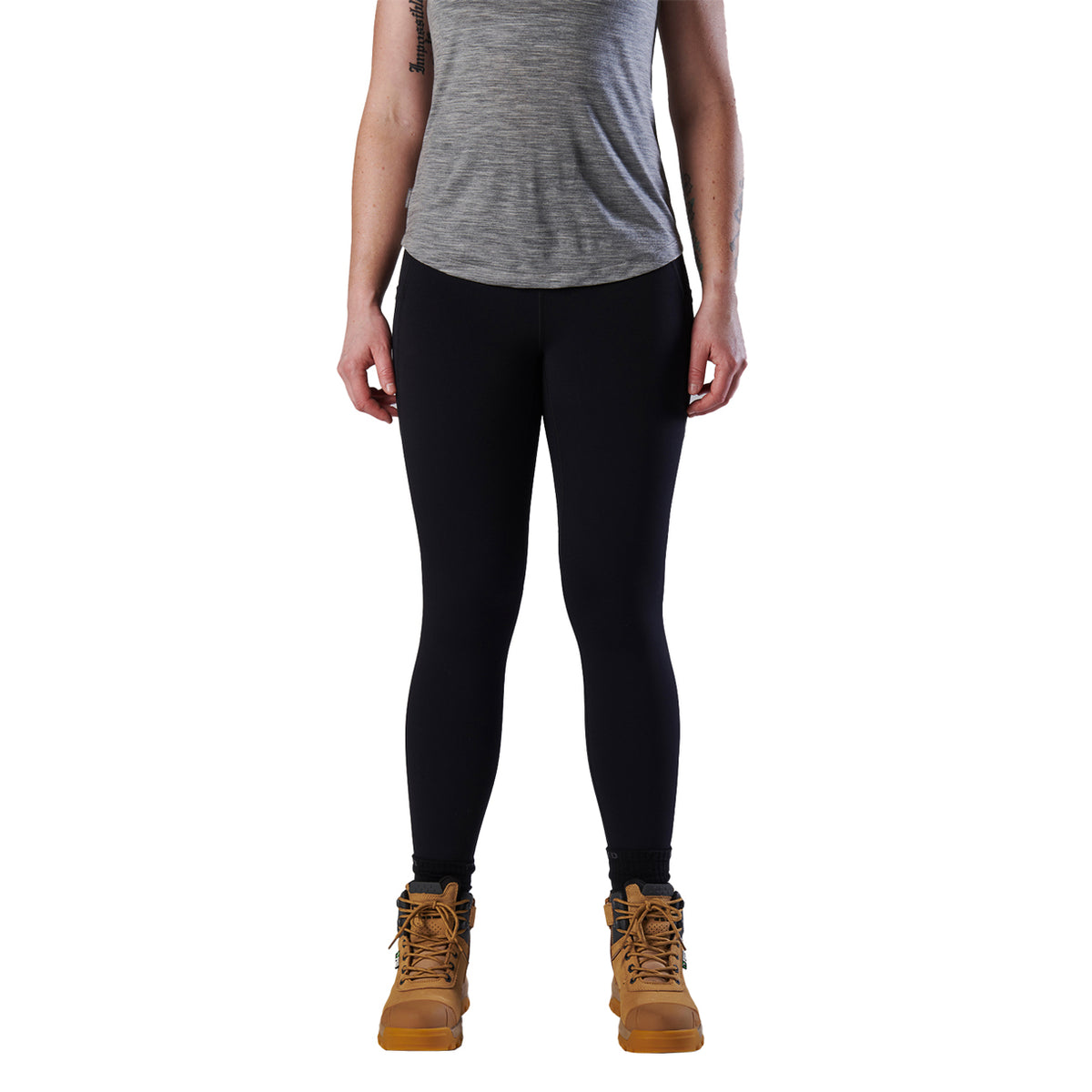 A woman modelling a black pair of FXD Women's Work Leggings (WP-9W) paired with a grey tee and wheat coloured work boots against a white background.