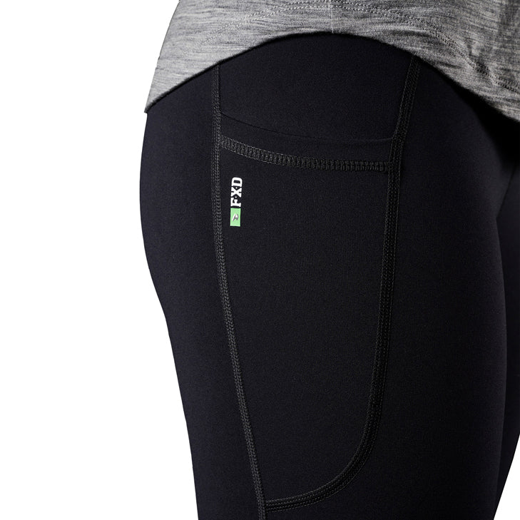 A close up of the side of a woman modelling a pair of black FXD Women's Work Leggings (WP-9W) showing pocket detail against a white background.
