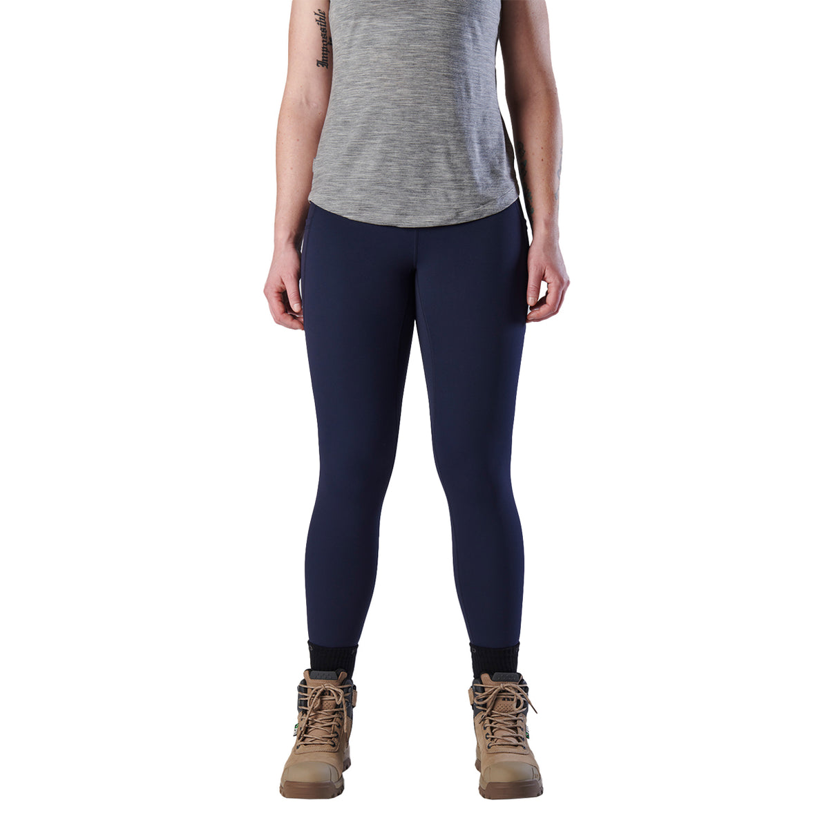 A woman modelling a pair of navy blue FXD Women's Work Leggings (WP-9W) paired with a grey tee and stone coloured work boots on a white background.