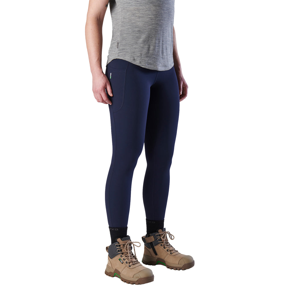 A 3-4 front view woman modelling a pair of navy blue FXD Women's Work Leggings (WP-9W) paired with a grey tee and stone coloured work boots on a white background.
