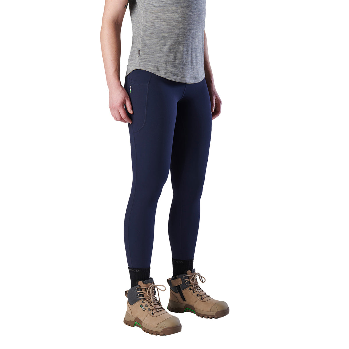 A 3-4 front view woman modelling a pair of navy blue FXD Women's Work Leggings (WP-9W) paired with a grey tee and stone coloured work boots on a white background.