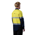A 3-4 back right view of a man wearing a yellow and navy FXD Men's LSH-4T Vented Tech Hi-Vis Long Sleeve Work Shirt (FX02504010) with hi vis tape and a pair of black work pants on a white background.