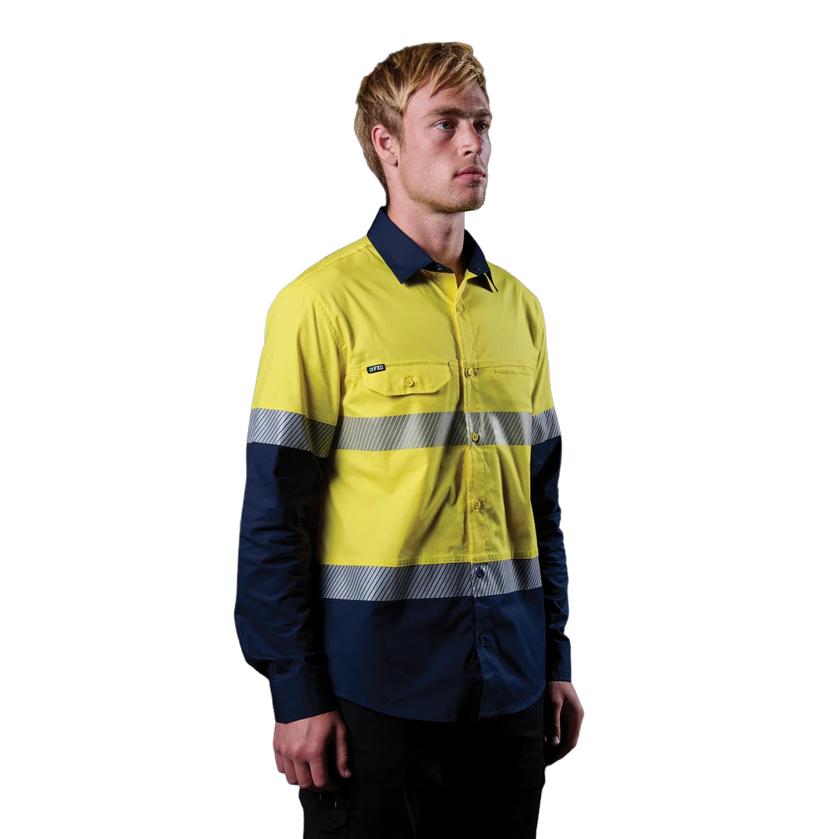A 3-4 right view of a man wearing a yellow and navy FXD Men's LSH-4T Vented Tech Hi-Vis Long Sleeve Work Shirt (FX02504010) with hi vis tape and a pair of black work pants on a white background.