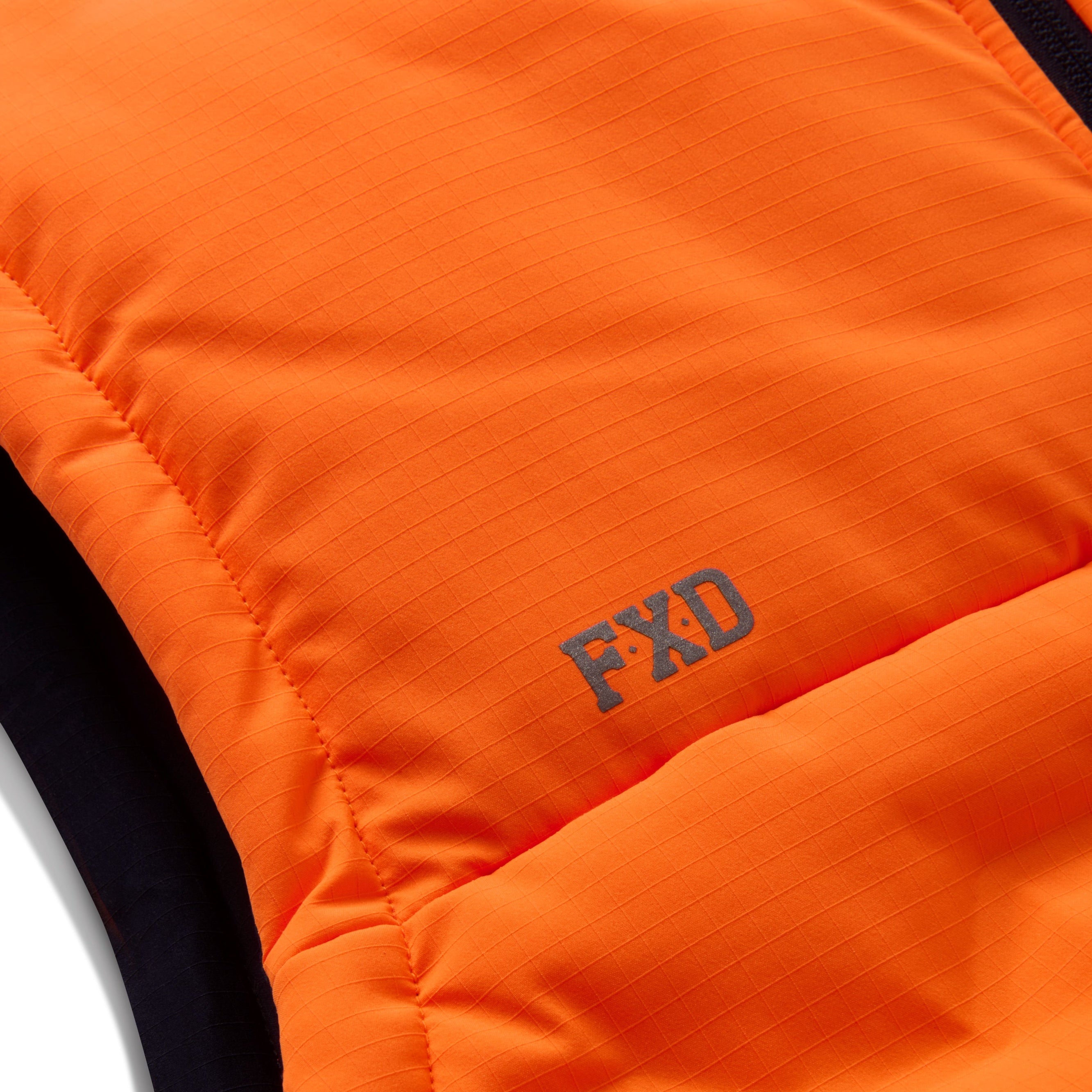 The FXD Mens WO-6 Puffer Vest (FX02407005) in bright orange features black side panels, front zipper, high collar, quilted padding, water-repellent finish, and FXD logo patches on the left chest and lower right.