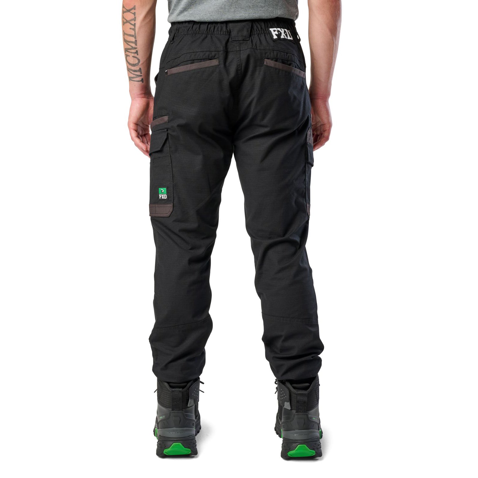A man wearing black cargo style FXD WP-12C Elastic Waist Stretch Ripstop Cuffed Work Pants (FX02506027) with a drawstring waist and black work boots, shown from the waist down on a plain white studio background, from behind.