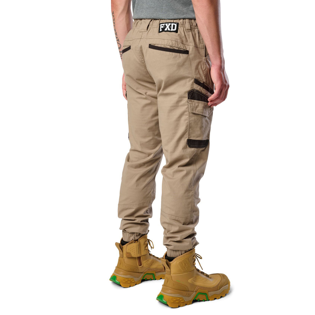 A 3-4 back view of a man wearing khaki cargo style FXD WP-12C Elastic Waist Stretch Ripstop Cuffed Work Pants (FX02506027) with a drawstring waist and wheat work boots, shown from the waist down on a plain white studio background.