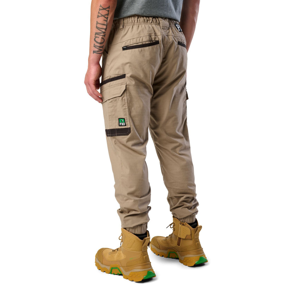 A 3-4 back view of a man wearing khaki cargo style FXD WP-12C Elastic Waist Stretch Ripstop Cuffed Work Pants (FX02506027) with a drawstring waist and wheat work boots, shown from the waist down on a plain white studio background.