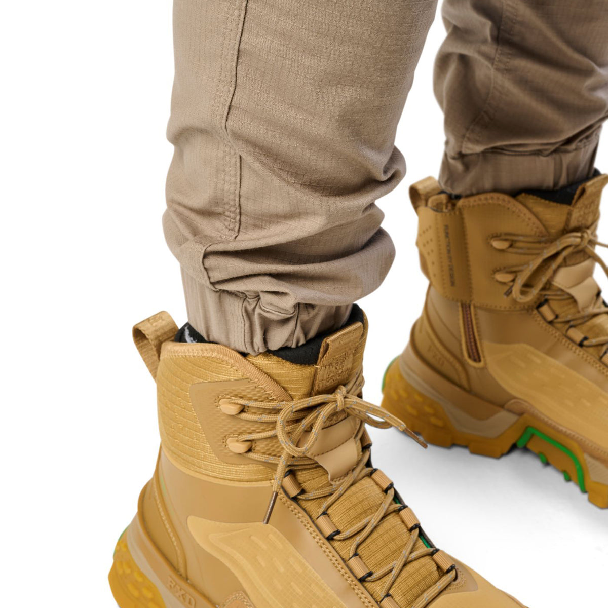 Cuff detail of a pair of khaki cargo style FXD WP-12C Elastic Waist Stretch Ripstop Cuffed Work Pants (FX02506027) and wheat work boots, on a plain white studio background.
