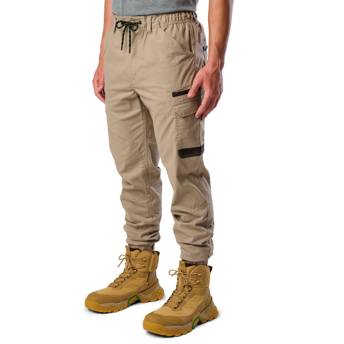 A 3-4 front view of a man wearing khaki cargo style FXD WP-12C Elastic Waist Stretch Ripstop Cuffed Work Pants (FX02506027) with a drawstring waist and wheat work boots, shown from the waist down on a plain white studio background.