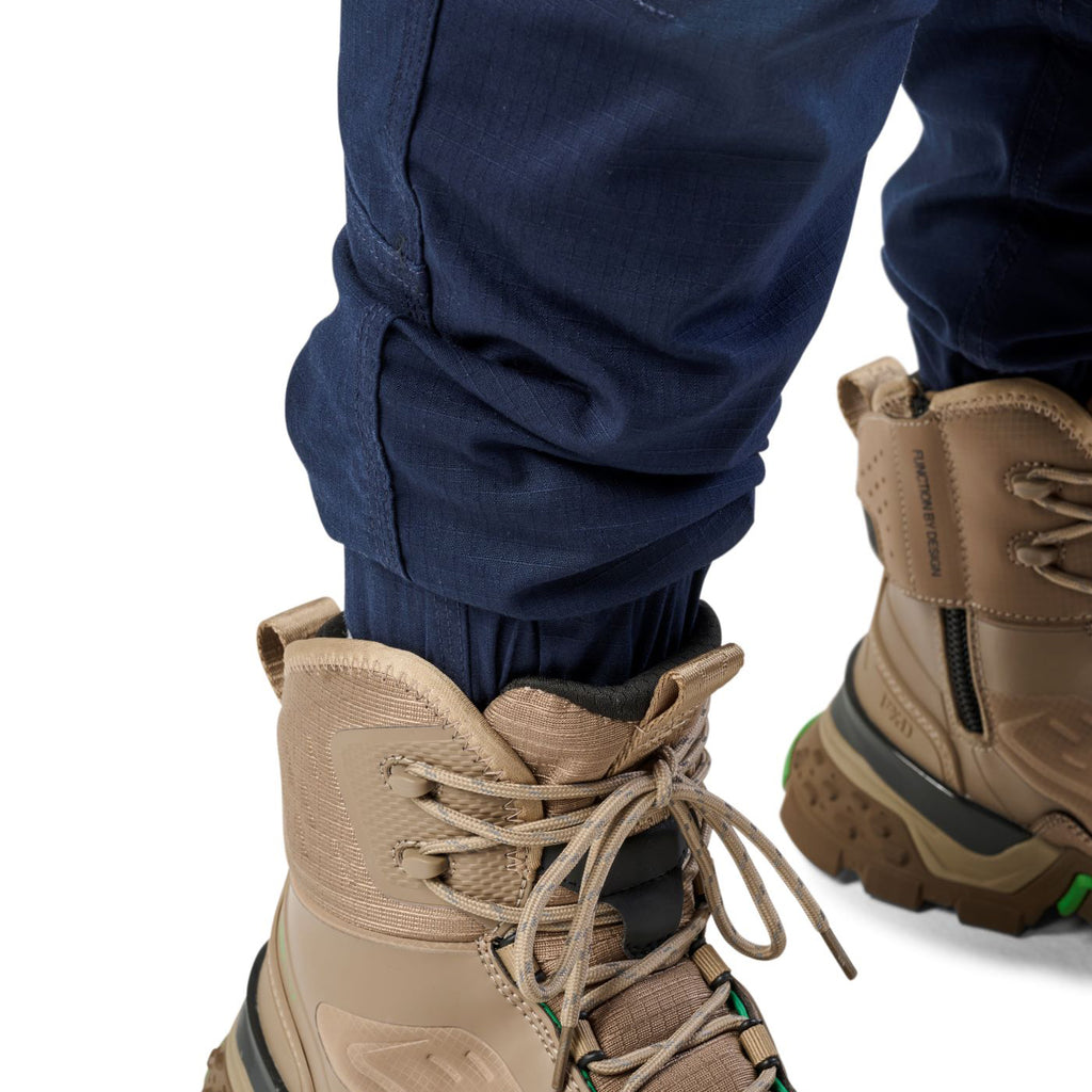 A close up of the cuff detail of a pair of navy cargo style FXD WP-12C Elastic Waist Stretch Ripstop Cuffed Work Pants (FX02506027) and stone work boots, on a plain white studio background.