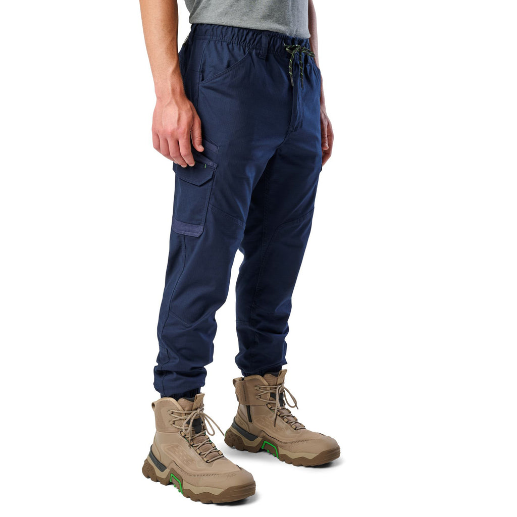 A 3-4 front view of a man wearing navy cargo style FXD WP-12C Elastic Waist Stretch Ripstop Cuffed Work Pants (FX02506027) with a drawstring waist and stone work boots, shown from the waist down on a plain white studio background.