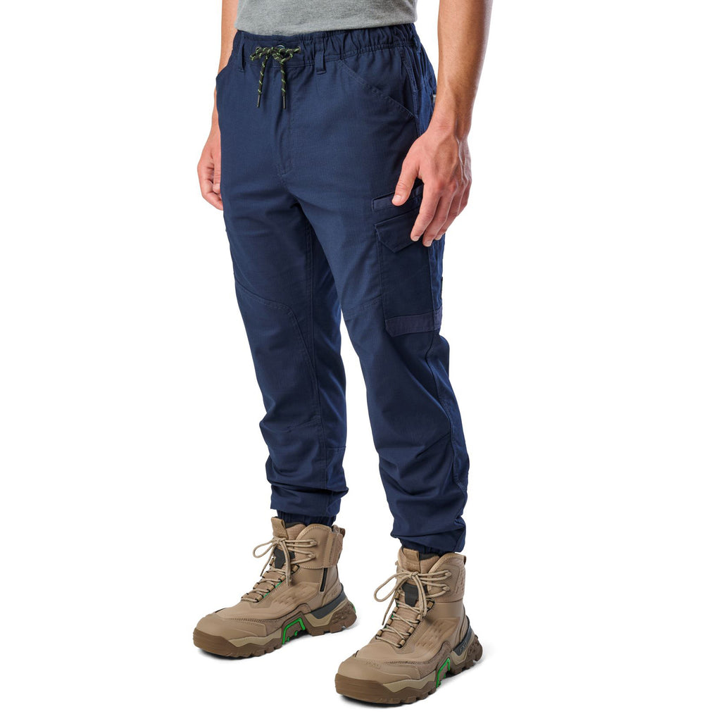 A 3-4 front view of a man wearing navy cargo style FXD WP-12C Elastic Waist Stretch Ripstop Cuffed Work Pants (FX02506027) with a drawstring waist and stone work boots, shown from the waist down on a plain white studio background.