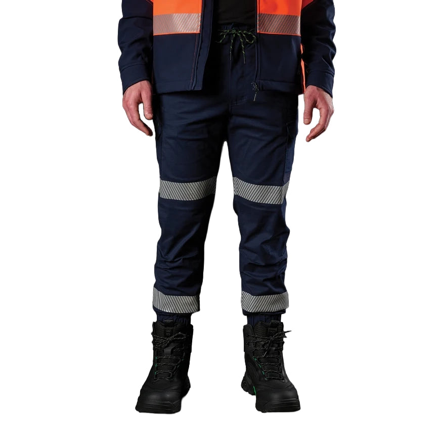 A man wearing navy FXD Men's WP-12CT Elastic Waist Stretch Ripstop Cuffed Taped Work Pants (FX02606029) with reflective tape at the knees and cuffs, paired with a matching navy and orange high-vis jacket and black boots, on a white background.
