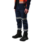 A 3-4 view of a man wearing navy FXD Men's WP-12CT Elastic Waist Stretch Ripstop Cuffed Taped Work Pants (FX02606029) with reflective tape at the knees and cuffs, paired with a matching navy and orange high-vis jacket and black boots, on a white background.