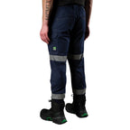 A 3-4 view of a man wearing navy FXD Men's WP-12CT Elastic Waist Stretch Ripstop Cuffed Taped Work Pants (FX02606029) with reflective tape at the knees and cuffs, paired with a matching navy and orange high-vis jacket and black boots, on a white background.