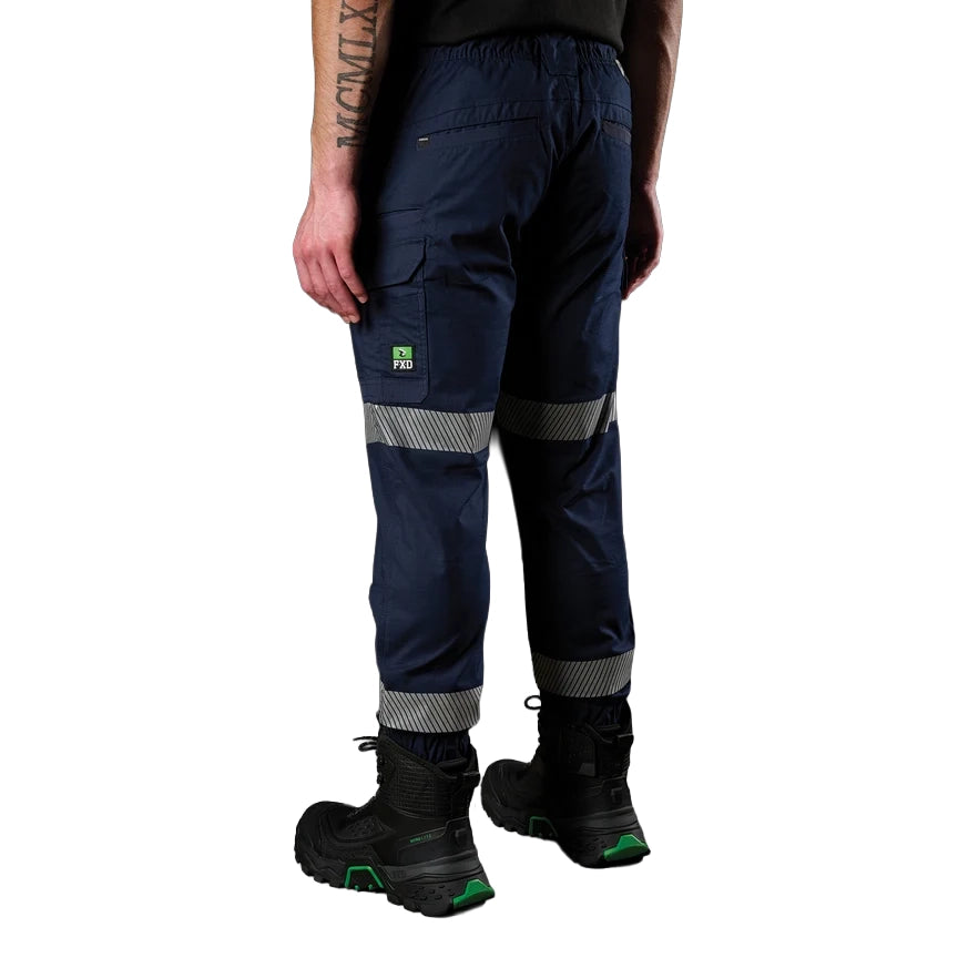 A 3-4 view of a man wearing navy FXD Men's WP-12CT Elastic Waist Stretch Ripstop Cuffed Taped Work Pants (FX02606029) with reflective tape at the knees and cuffs, paired with a matching navy and orange high-vis jacket and black boots, on a white background.