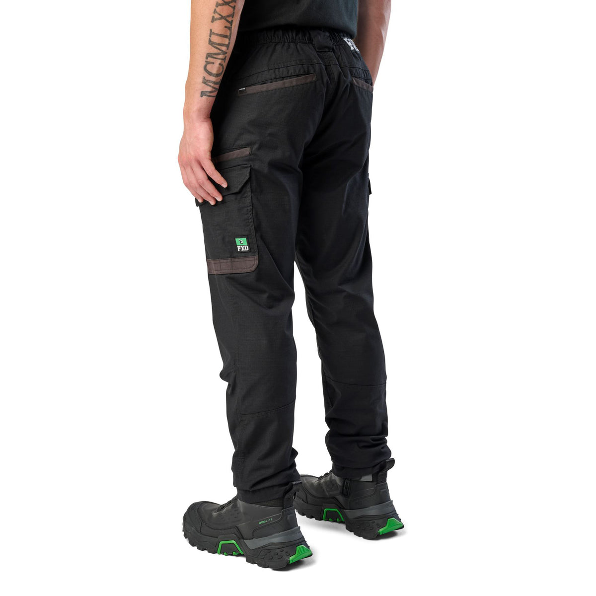 A 3-4 back view of a man wearing black cargo style FXD Men's WP-12 Elastic Waist Stretch Ripstop Work Pants (FX02506026) with black work boots on a white background.