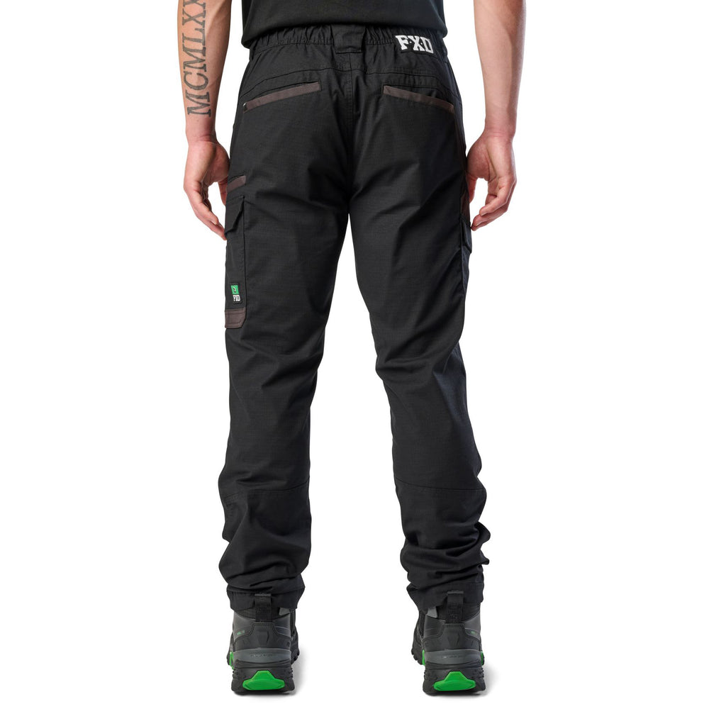 A back view of a man wearing black cargo style FXD Men's WP-12 Elastic Waist Stretch Ripstop Work Pants (FX02506026) with black work boots on a white background.