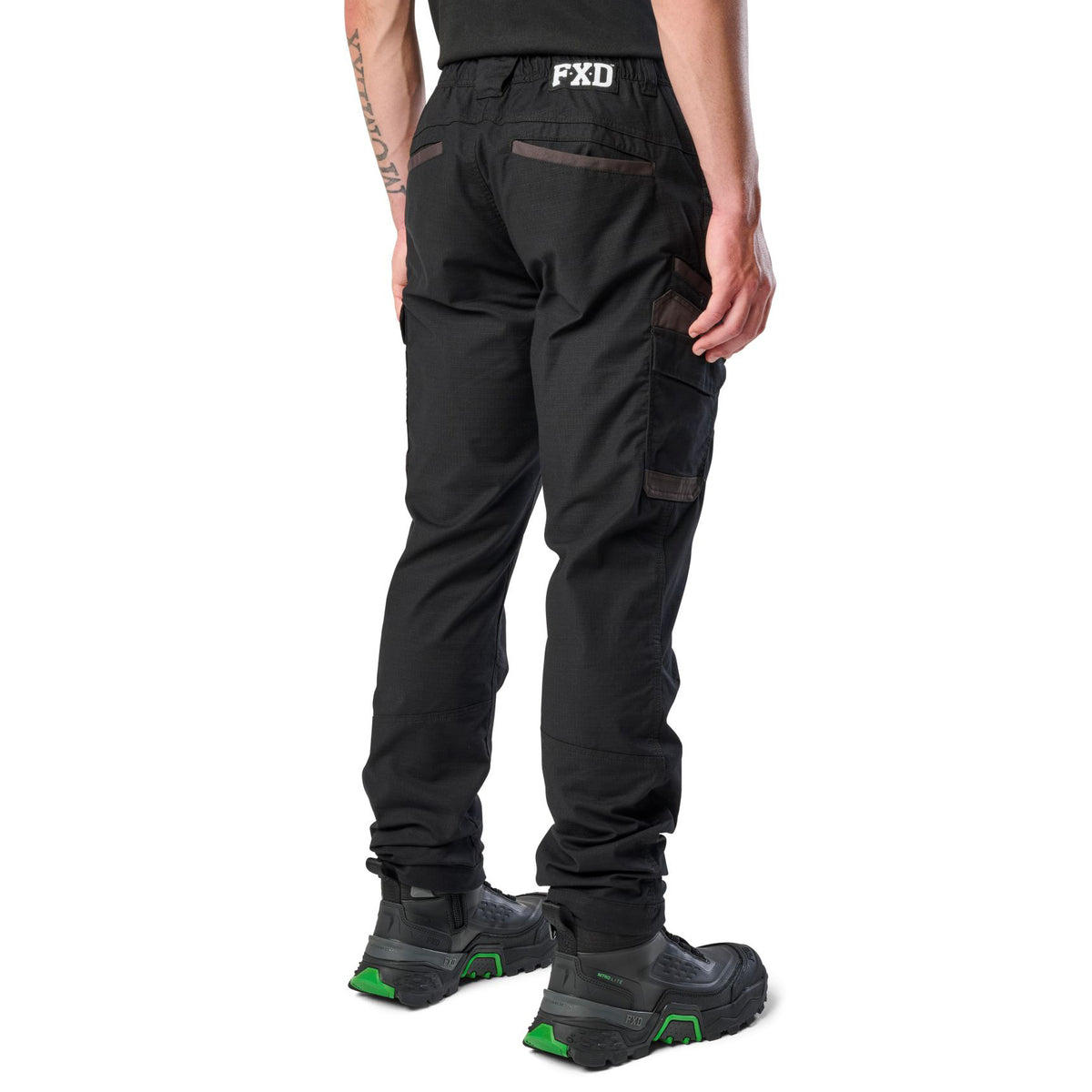A 3-4 back view of a man wearing black cargo style FXD Men's WP-12 Elastic Waist Stretch Ripstop Work Pants (FX02506026) with black work boots on a white background.